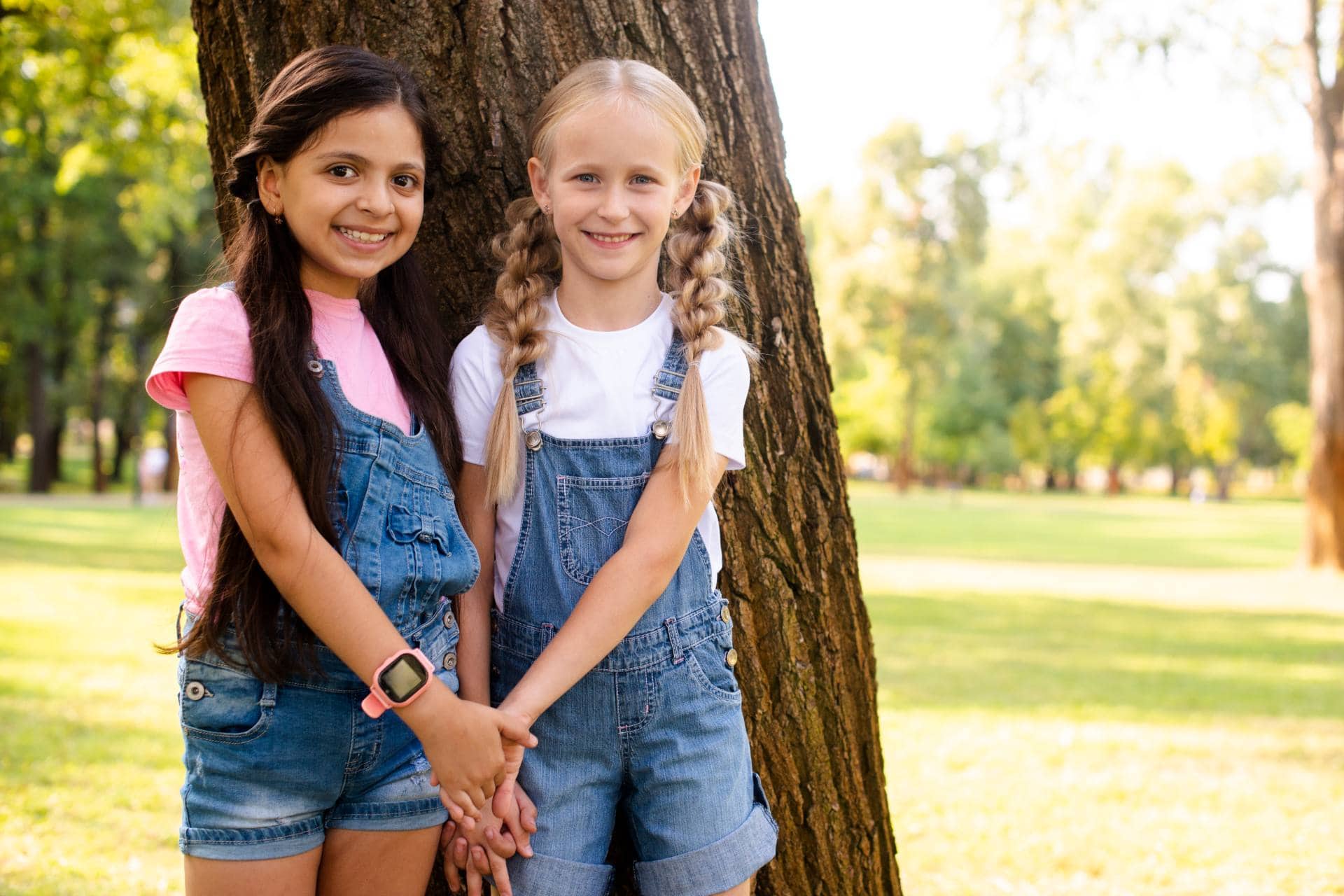 Two girls smiling with matching overalls after two phase treatment at Ward Orthodontics.